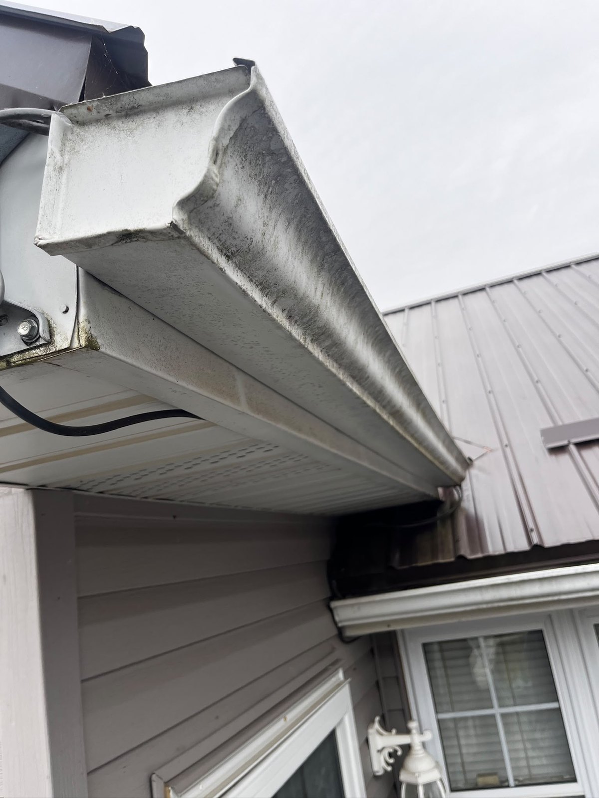 Eavestrough face streaked black with oxidation and road film before cleaning