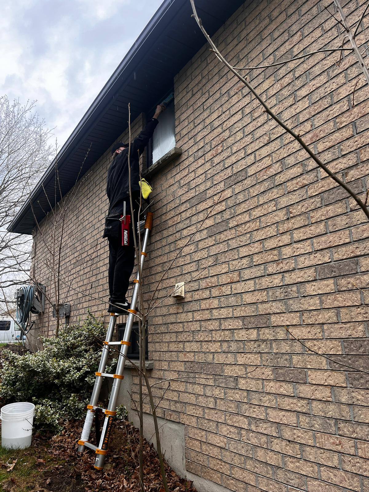 Ladder against a brick home, working along the roofline