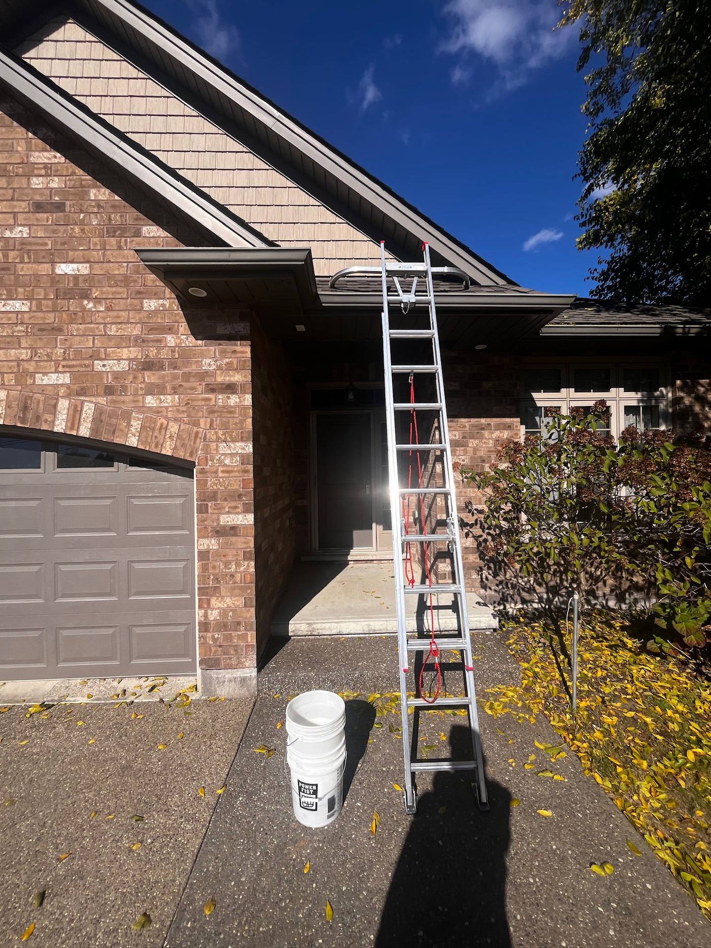 Ladder and bucket set up at the eaves during a fall gutter clean